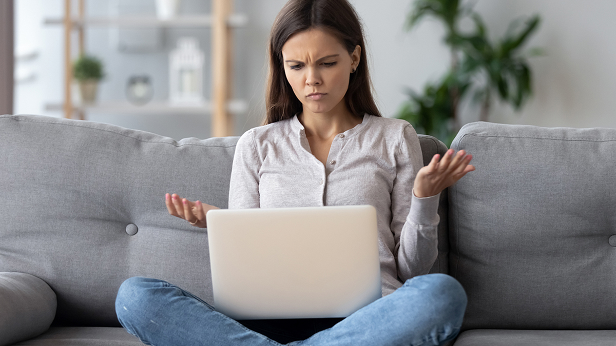 Woman sitting on couch looking at laptop screen confused.