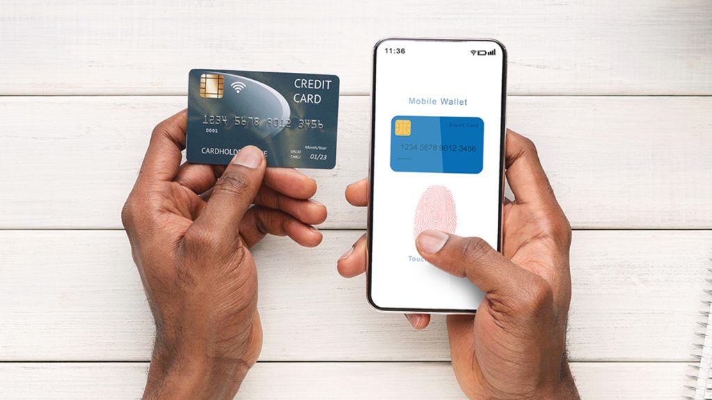 Top View Of Man Holding Cellphone And Credit Card Showing Mobile Wallet App Using Biometric Thumb Print For MultiFactor Authentication As Part Of A Cybersecurity Program To Keep Data Safe.