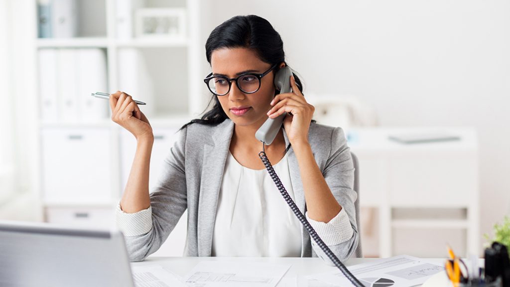 Business, technology, communication - businesswoman with papers calling on VoIP phone at office.