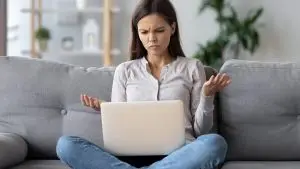 Confused young woman looking on laptop needing tech support because her wi-fi network is not working.