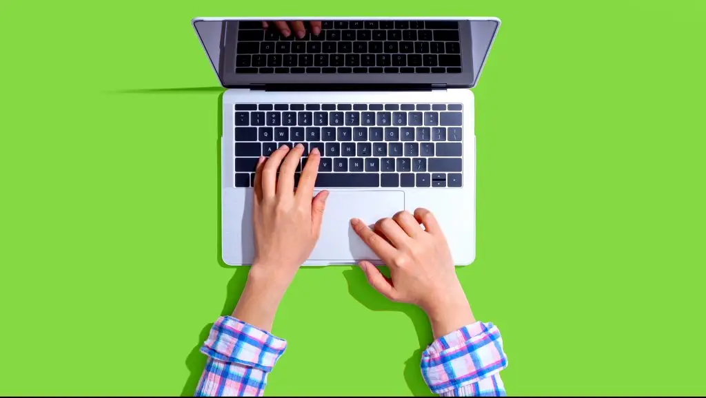 hands typing on laptop keyboard on green background