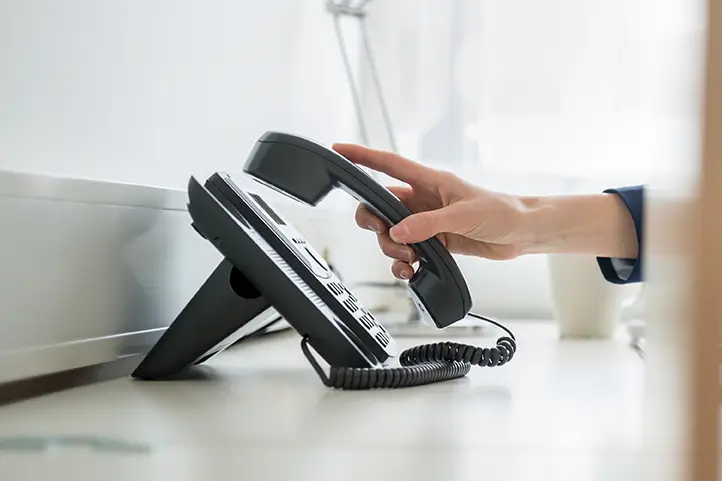 User answering desktop VoIP phone on work desk.
