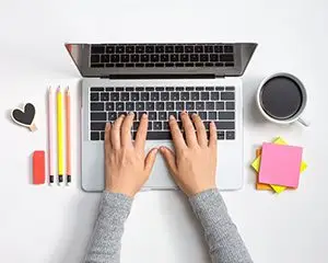 Person using a laptop computer with office supplies and coffee