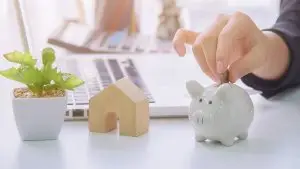 User dropping coins in piggy bank next to laptop on work desk.