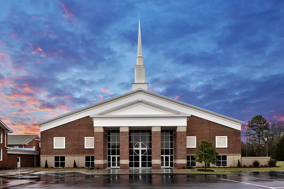 Exterior of modern brick church with white steeple at sunset