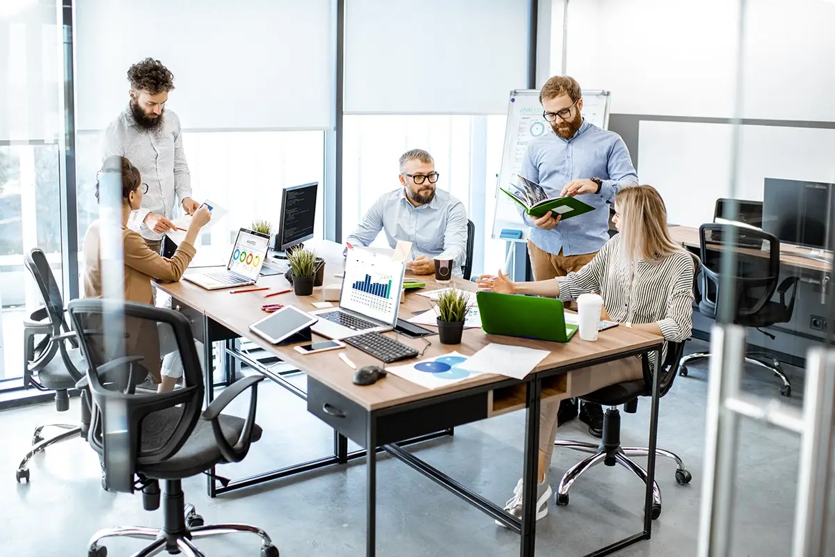 Busy office employees using computers, laptops and tablets getting tech support from an IT Engineer