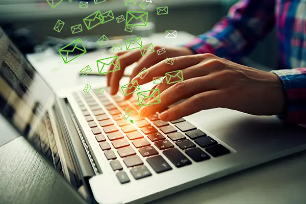 hands typing on laptop keyboard with green email envelopes while business person is checking their work email.