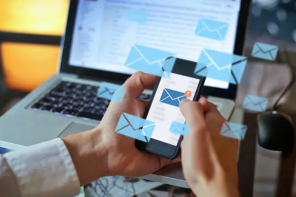 hands holding smart phone over laptop keyboard while checking email.