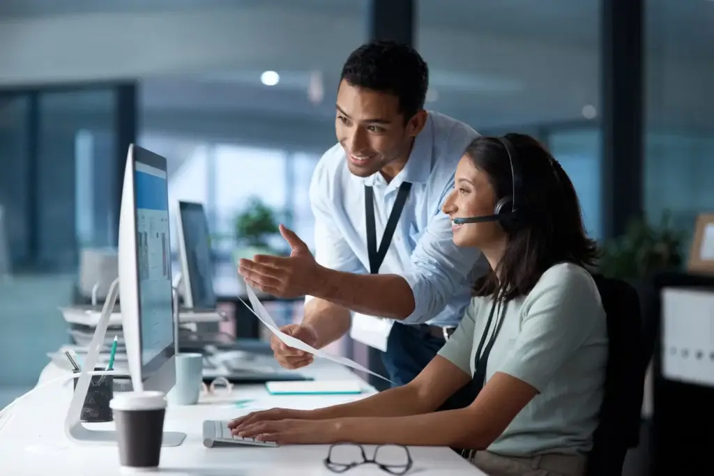 IT Technician providing IT Support to Help Desk Agent. Both are viewing the Help Desk Agent's computer and smiling.