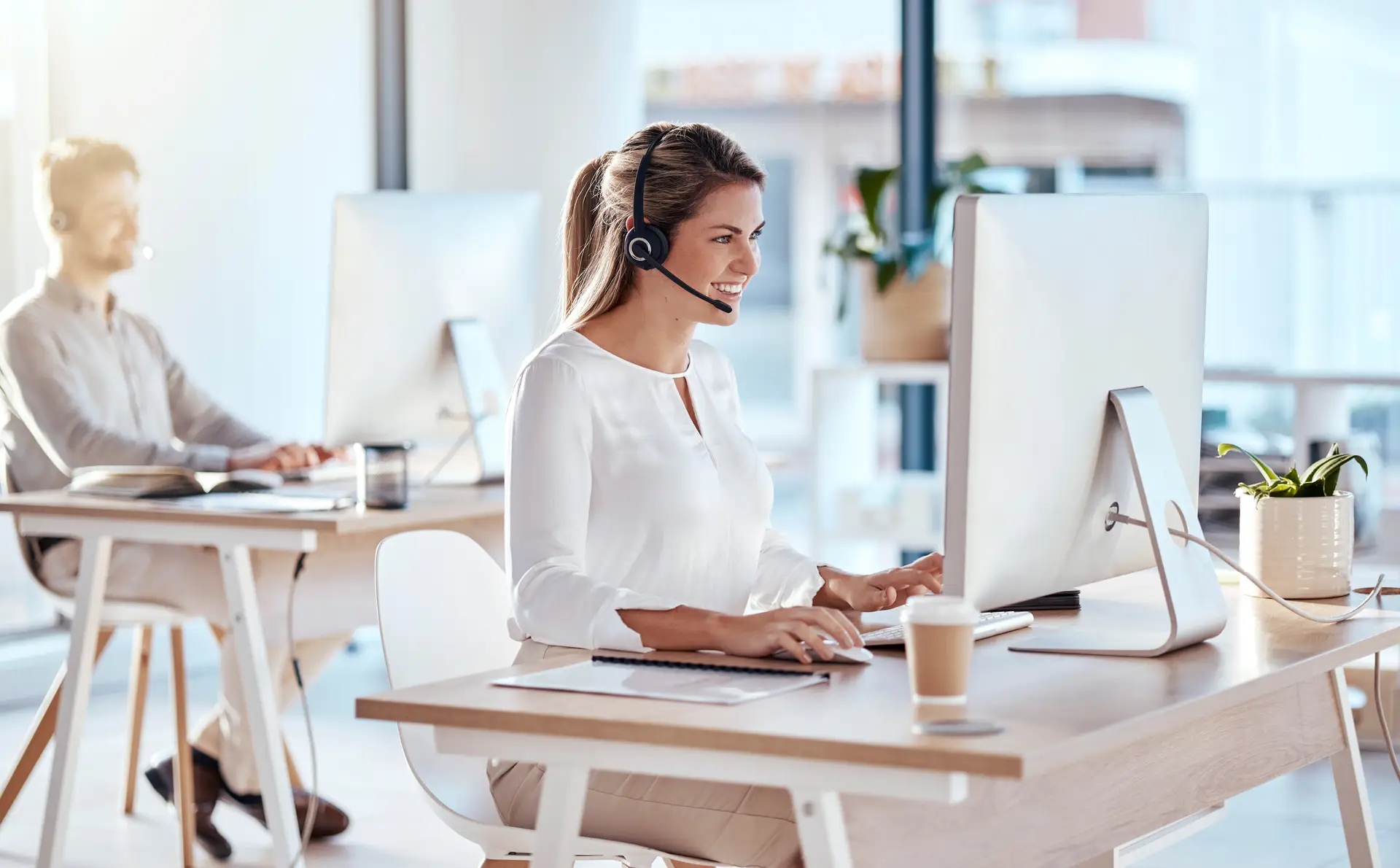 Caucasion woman working in call center wearing headset and looking at her workstation monitor.