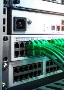 network equipment on a data rack with green data cables plugged in