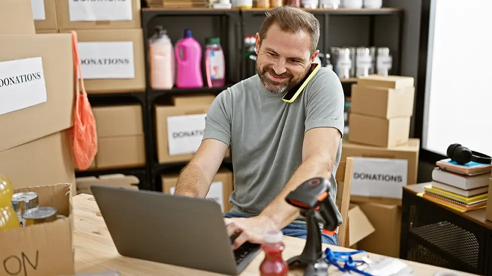 Caucasion male volunteering for a nonprofit organization using a VoIP phone system that integrates with smart phones and laptop computer while accepting donation boxes.